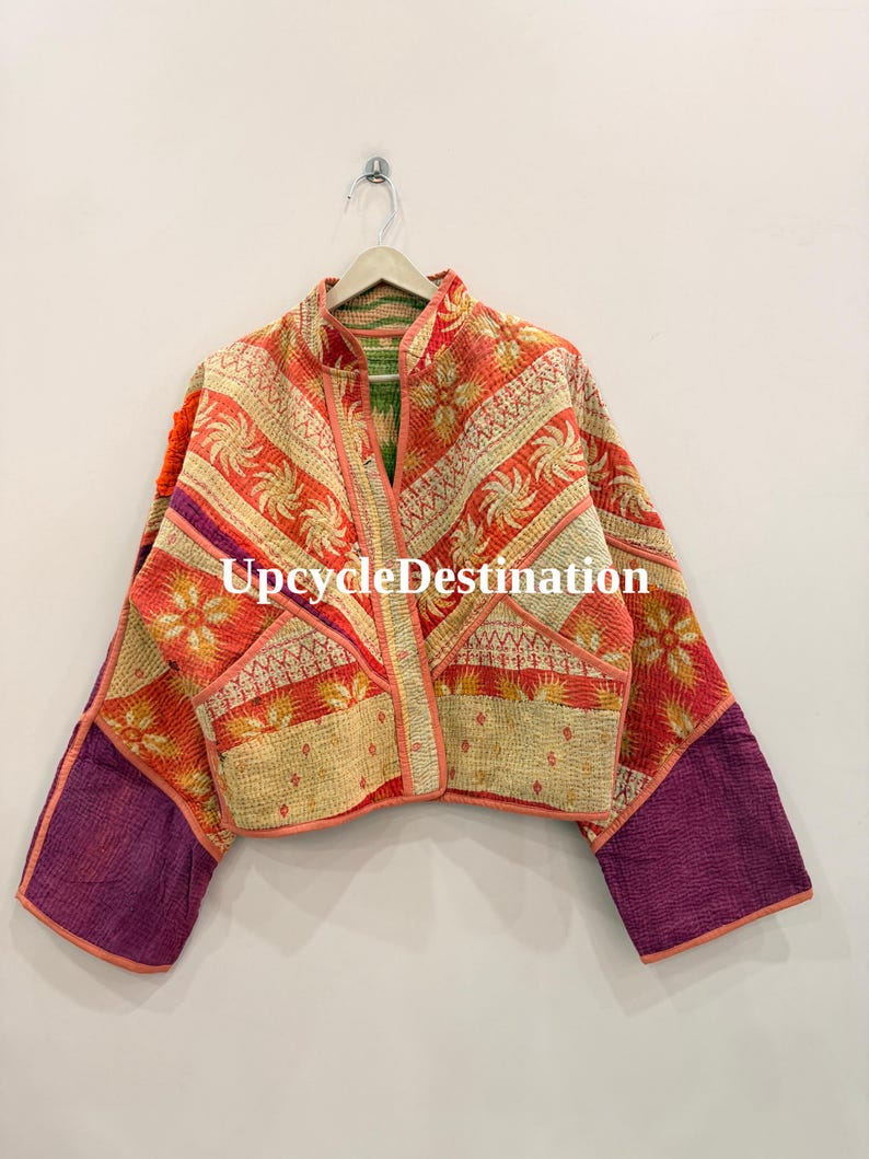 May include: A cropped jacket featuring a patchwork design with orange, red, and cream floral patterns, accented by solid purple sleeves and orange trim. The garment has a stand-up collar and is displayed on a hanger with the text UpcycleDestination.