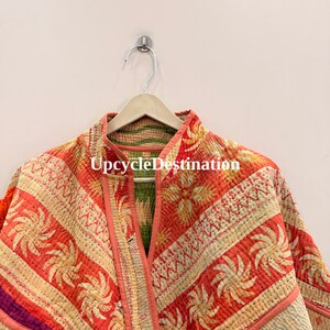 May include: A quilted jacket featuring a vibrant orange and cream color palette with repeating sunburst patterns and floral motifs. The garment has a mandarin collar, visible kantha-style stitching, and the text UpcycleDestination printed.