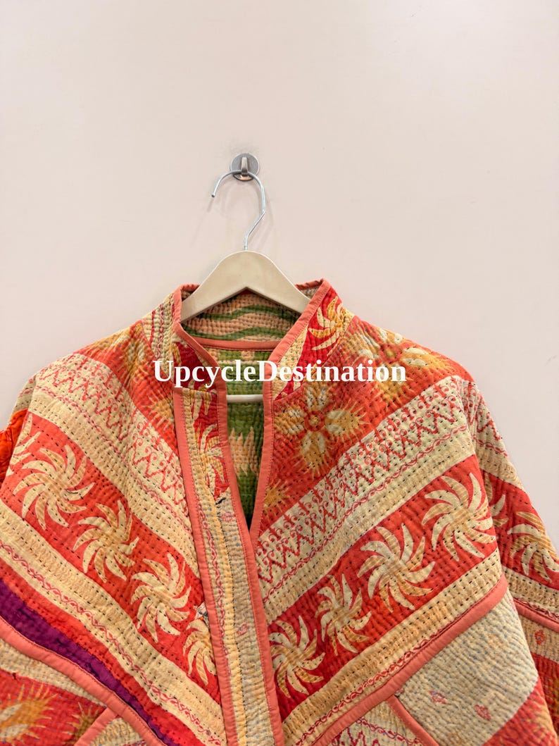 May include: A quilted jacket featuring a vibrant orange and cream color palette with repeating sunburst patterns and floral motifs. The garment has a mandarin collar, visible kantha-style stitching, and the text UpcycleDestination printed.