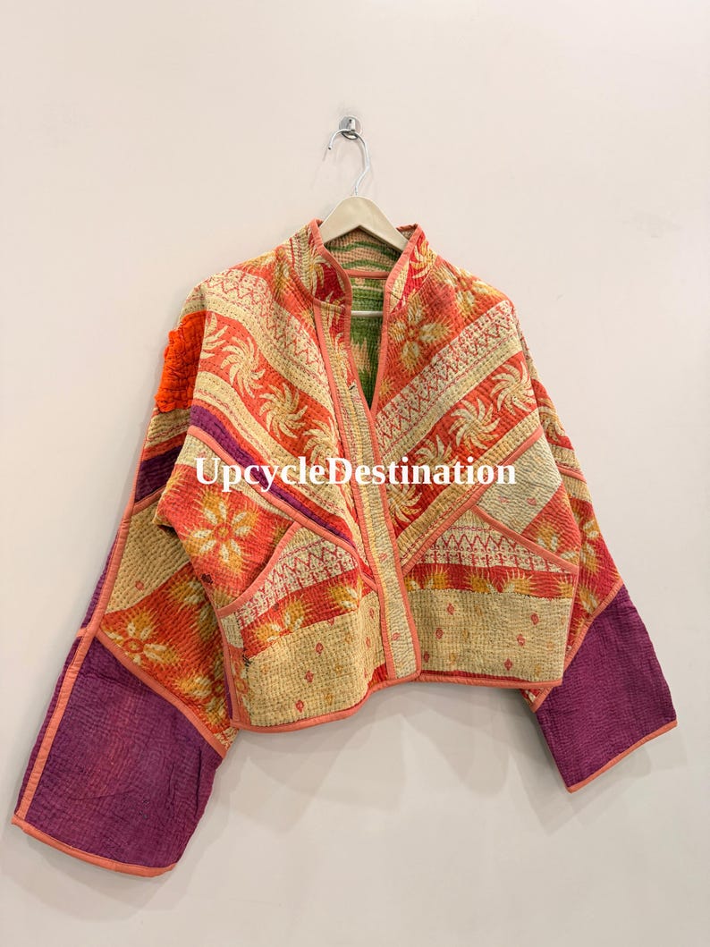 May include: A quilted jacket featuring a patchwork design with orange, cream, and purple fabric panels. The garment displays intricate floral and geometric patterns, a stand-up collar, long sleeves, and the text UpcycleDestination printed centrally.
