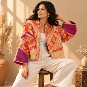 May include: A quilted jacket featuring a patchwork design with vibrant orange, red, and purple panels. The garment displays intricate floral and geometric embroidery patterns, wide sleeves, and an open front, paired with plain white wide-leg trousers.