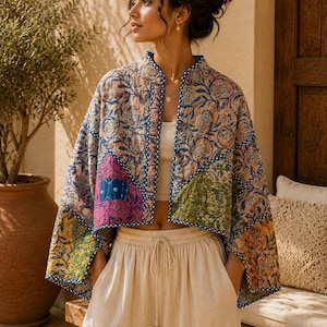 May include: A cropped quilted jacket featuring a patchwork design with floral patterns in shades of blue, pink, yellow, and green. The jacket has a mandarin collar, wide sleeves, and blue and white patterned trim along the edges and front opening.