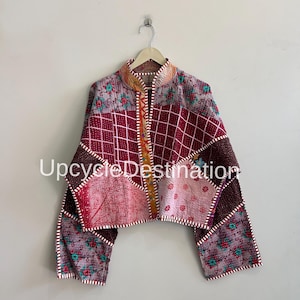 Puede incluir: Chaqueta patchwork con cuello alto y mangas largas. La chaqueta presenta una variedad de patrones, incluyendo diseños florales, geométricos y de hojas, en tonos burdeos, rosa y morado. El texto "UpcycleDestination" es visible.