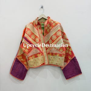 May include: A quilted jacket featuring a patchwork design with orange, cream, and purple fabric panels. The garment has long sleeves, a front opening, and visible stitching throughout. The text UpcycleDestination is printed across the center.