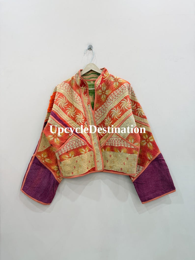 May include: A quilted jacket featuring a patchwork design with orange, cream, and purple fabric panels. The garment has long sleeves, a front opening, and visible stitching throughout. The text UpcycleDestination is printed across the center.