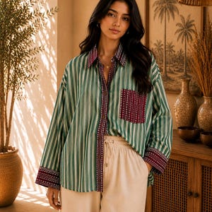 May include: A long-sleeved button-down shirt featuring vertical green and white stripes, accented with a dark maroon patterned collar, front placket, chest pocket, and cuffs. The shirt is paired with light beige, high-waisted, wide-leg trousers.