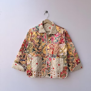 May include: A quilted jacket featuring a patchwork design of floral patterns in shades of yellow, pink, and green. The jacket includes a collar, long sleeves with striped cuffs, and two front pockets with small red heart embroidery details.