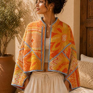 Peut inclure: Une veste courte ouverte sur le devant, dotée d'un motif matelassé orange et jaune vif avec des détails géométriques et floraux. Le vêtement est bordé d'un liseré rayé bleu clair et blanc le long des bords, du col et des manches larges.