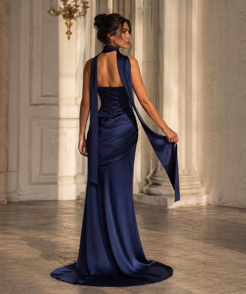 May include: A navy blue satin gown with a halter neckline and a flowing skirt. The dress features a corset-style bodice and a long, draped sash. The elegant design is suitable for formal events.