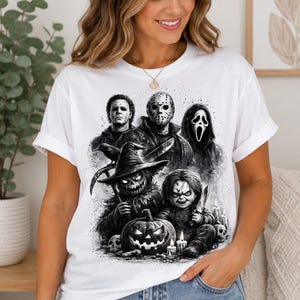 Puede incluir: Una camiseta blanca de manga corta con un estampado gráfico detallado en blanco y negro de varios personajes de películas de terror, incluyendo una figura enmascarada, un espantapájaros, una calabaza y una muñeca, dispuestos en estilo collage.