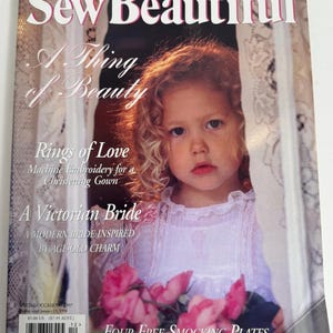 May include: The cover of "Sew Beautiful" magazine shows a young girl with curly hair, wearing a white dress and holding pink roses. The magazine's title and issue details are visible, with text about patterns and a Victorian bride theme.