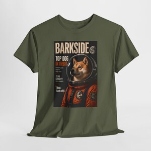 May include: Olive green t-shirt featuring a graphic of a Shiba Inu dog in an astronaut suit. The graphic includes the text "BARKSIDE TOP DOG IN ORBIT" and other phrases. The dog is in a space helmet, with a moon in the background.