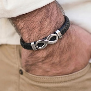 May include: A black braided leather bracelet featuring a silver-toned infinity symbol centrepiece. The metal components are engraved with the names Jackson and Lucilla, and the centre of the infinity loop is engraved with the text Forever Love.