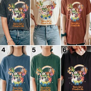 K&ouml;nnte beinhalten: Sechs verschiedenfarbige T-Shirts mit einer Grafik von Toy Story-Charakteren in Form von Mickey Mouse-Ohren, einem Regenbogen und dem Text "You've Got a Friend in Me". Die Farben sind Anthrazit, Creme, Rost, Blau, Gr&uuml;n und Schwarz.