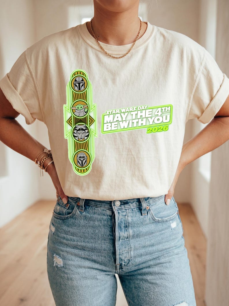 Pu&ograve; includere: T-shirt color crema con grafica verde neon con personaggi di Star Wars e la scritta "STAR WARS DAY MAY THE 4TH BE WITH YOU 2026". La maglietta &egrave; abbinata a jeans azzurri.