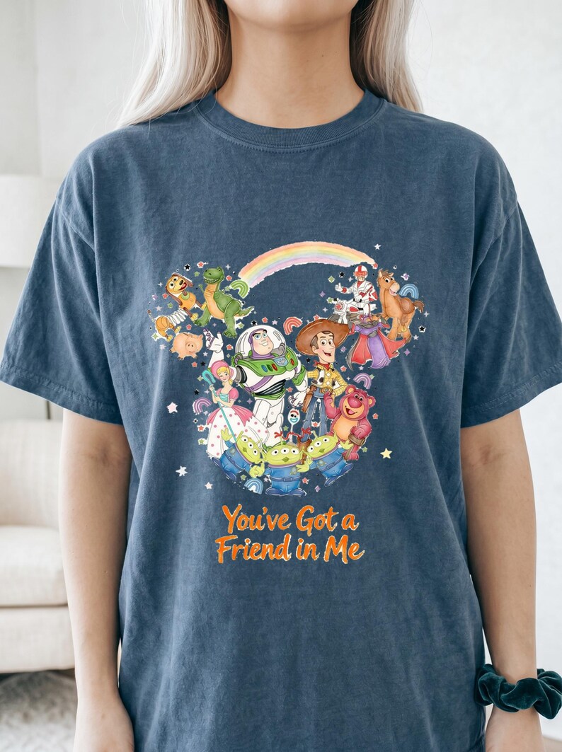 K&ouml;nnte beinhalten: Marineblaues T-Shirt mit einer farbenfrohen Grafik von Toy Story-Charakteren, angeordnet in Form eines Mickey Mouse-Kopfes. Der Text "You've Got a Friend in Me" ist orangefarben gedruckt.