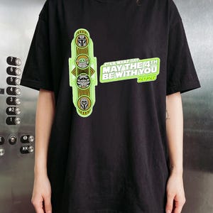 Pu&ograve; includere: T-shirt nero con un design del Star Wars Day. Il design include illustrazioni di personaggi e la scritta "MAY THE 4TH BE WITH YOU 2020". La grafica &egrave; verde e gialla. Un capo d'abbigliamento casual.