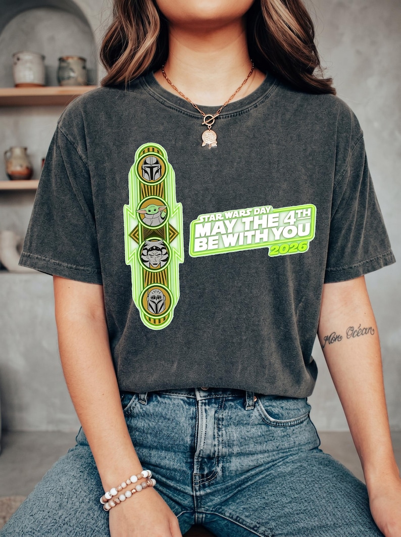 Pu&ograve; includere: T-shirt grigio scuro con grafica verde neon con personaggi di Star Wars e la scritta "STAR WARS DAY MAY THE 4TH BE WITH YOU 2026". La maglietta ha girocollo e maniche corte.