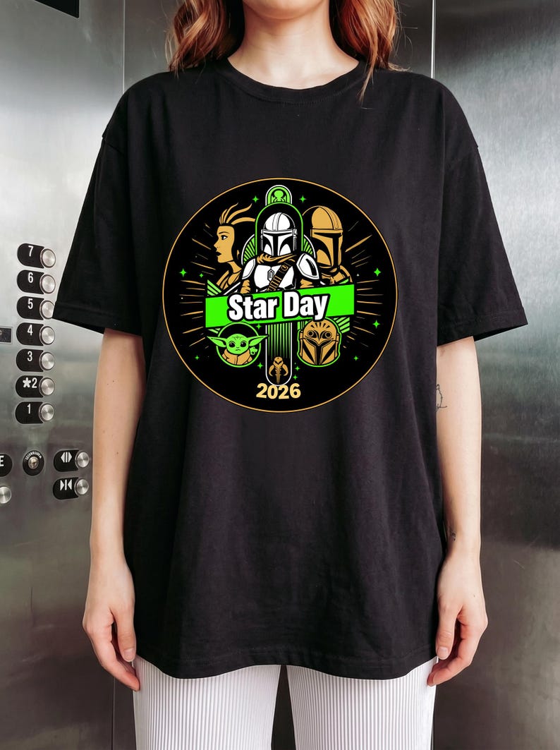 May include: Black t-shirt featuring a circular graphic with characters and the text "Star Day 2026". The design includes images of a Mandalorian, Grogu, and other characters from the Star Wars franchise. The graphic is in green, white, and gold.