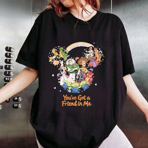 K&ouml;nnte beinhalten: Schwarzes T-Shirt mit einem farbenfrohen Motiv von Disney's Toy Story-Charakteren in Form eines Mickey Mouse-Kopfes, mit einem Regenbogen und dem orangefarbenen Text "You've Got a Friend in Me".