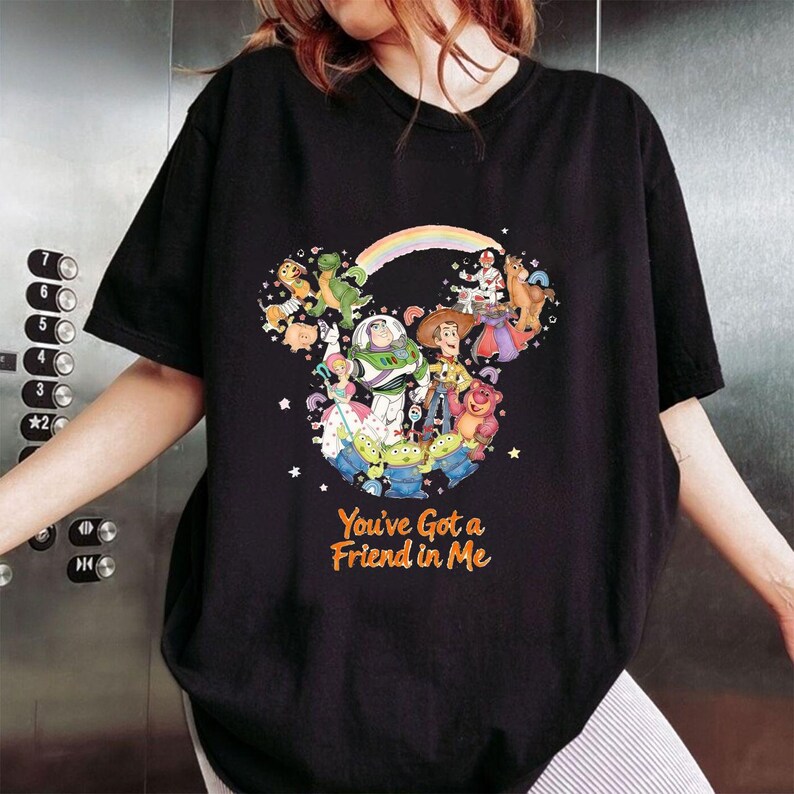 K&ouml;nnte beinhalten: Schwarzes T-Shirt mit einem farbenfrohen Motiv von Disney's Toy Story-Charakteren in Form eines Mickey Mouse-Kopfes, mit einem Regenbogen und dem orangefarbenen Text "You've Got a Friend in Me".