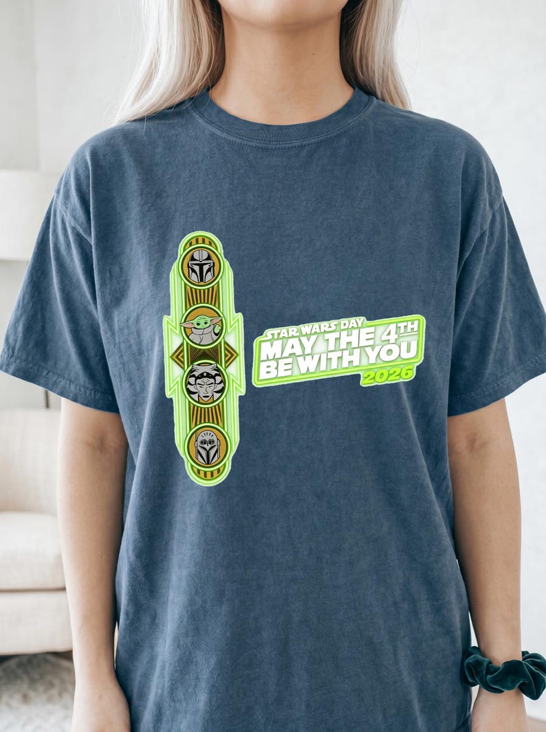 Pu&ograve; includere: T-shirt blu con grafica verde neon con personaggi di Star Wars e la scritta "STAR WARS DAY MAY THE 4TH BE WITH YOU 2026". La grafica include immagini dei personaggi del franchise di Star Wars.