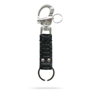 Puede incluir: Un llavero de cuero negro con un mosquetón y un llavero de metal plateado. El cuero tiene un patrón texturizado en forma de escamas. El mosquetón es giratorio para facilitar la fijación.