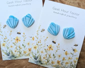 May include: A pair of blue and white seashell-shaped earrings on a white card with the text "Geek Hour Factor handcrafted jewellery".