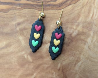 May include: A pair of black dangle earrings with three heart-shaped charms in red, yellow, and green.