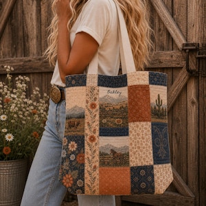 May include: A quilted tote bag featuring a patchwork design of various fabric panels. The panels display scenes of mountains, a horse, a cow, a cactus, and floral patterns in shades of blue, orange, and cream. The name Oakley is embroidered.