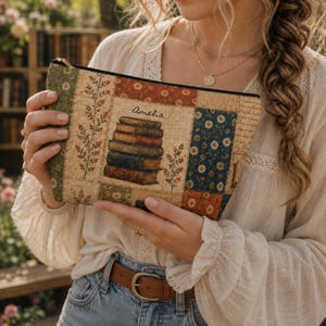 Puede incluir: Un estuche rectangular con cremallera que presenta un estampado estilo patchwork con varios patrones, incluyendo motivos florales, texto manuscrito y una ilustración central de una pila de cinco libros con el nombre Amelia impreso en cursiva negra.