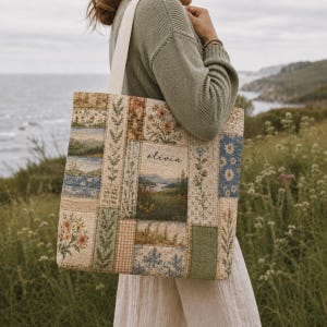 Peut inclure: Un sac fourre-tout rectangulaire présentant un motif patchwork composé de diverses scènes florales et paysagères dans des tons terreux. Le panneau central affiche un paysage imprimé avec le nom olivia en écriture noire et deux larges anses.