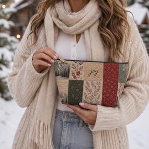 May include: A rectangular zippered pouch featuring a patchwork design of various winter-themed fabrics, including mountain landscapes, floral patterns, and red snowflake prints. The center panel displays the word joy in a cursive black script font.