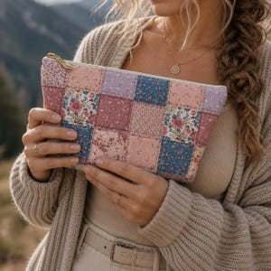 May include: A rectangular zippered pouch featuring a quilted patchwork design composed of various fabric squares in shades of dusty pink, mauve, and navy blue, each decorated with small floral patterns and a gold-toned metal zipper pull.