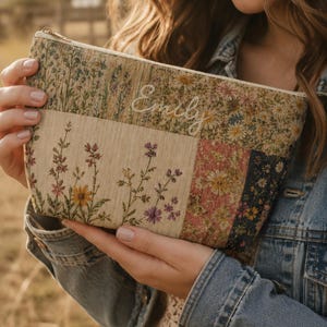 May include: A rectangular zippered pouch featuring a patchwork design of floral patterns in shades of beige, pink, yellow, and blue. The upper section includes the embroidered name Emily in white script. The fabric has a textured, woven appearance.
