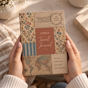 Pode incluir: Um diário de viagem retangular com uma capa de patchwork apresentando padrões florais, listras azuis e um mapa-múndi. O painel central é de cor ferrugem com o texto 'LYDIA'S Travel Journal'. O texto adicional inclui 'THE WORLD AWAITS' e 'New Places, Endless Stories, Open Roads, Great Memories'.