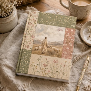 Könnte beinhalten: Ein Notizbuch mit festem Einband und einem Patchwork-Stoffbezug mit Blumenmuster in Grün-, Rosa- und Cremetönen. Das mittlere Feld zeigt eine gedruckte Illustration einer Person in einem Gewand, die mit einer Schafherde über ein Feld geht, mit dem Namen Lydia.