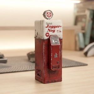 Può includere: Una replica rettangolare di distributore automatico rosso e bianco con la scritta Drink Jugger-Nog, un emblema circolare superiore con un'icona a forma di fulmine, una fessura per monete e un display digitale che mostra 100. Finitura usurata.