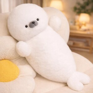 May include: A plush white seal stuffed animal with a round head, small black eyes, and a gray nose. The seal has small flipper-like arms and a tail. The toy is soft and fluffy, perfect for cuddling.