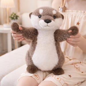 May include: A plush otter toy with brown fur, white chest, and a dark brown nose. The stuffed animal has outstretched arms and is sitting on a person's lap. The toy has a friendly expression and is designed to be cuddly.