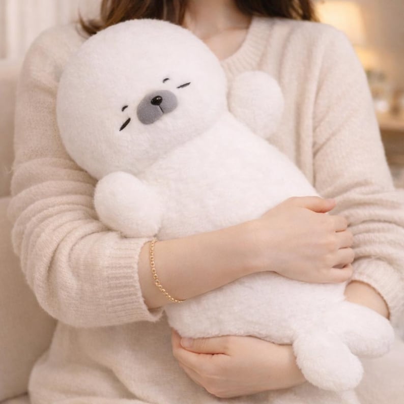 May include: A plush white seal stuffed animal with a round head, small black eyes, and a gray nose. The seal has small flipper-like arms and a long body. The plush toy is soft and fluffy, perfect for cuddling.
