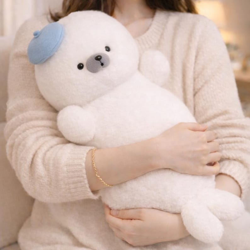 May include: A plush white seal toy with a light blue beret. The stuffed animal has a round body, small arms, and flipper-like feet. It has a gray nose and black eyes. The toy is soft and cuddly, perfect for children.
