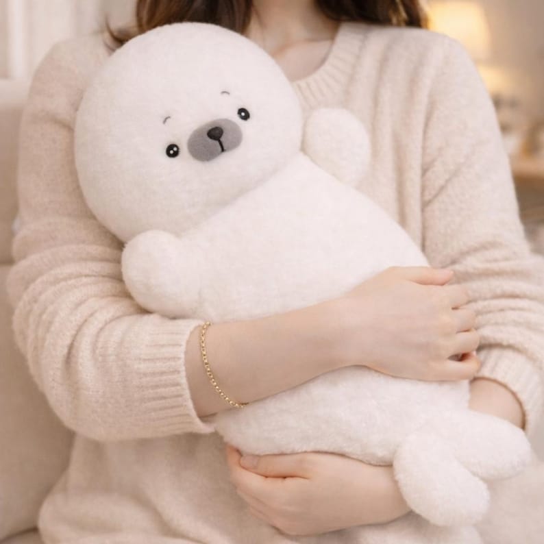 May include: A plush white seal stuffed animal with a round head, small arms, and flipper-like feet. The seal has a gray nose and black eyes. The toy is soft and cuddly, perfect for children or as a decorative item.
