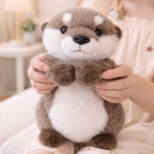 May include: A plush otter toy with a brown and white color scheme. The stuffed animal has a white belly, brown paws, and a brown head with white accents. The otter has a black nose and is being held by a person.