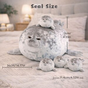 Pode incluir: Um brinquedo de pel&uacute;cia de foca em tons de cinza e branco, com um corpo grande e focas menores. A foca grande mede 36 cm de comprimento e 11 cm de altura. O texto "Seal Size" est&aacute; no topo.