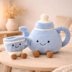 Puede incluir: Un juego de tetera y taza de peluche azul claro con caras sonrientes y pies marrones. La tetera tiene una tapa blanca y una banda blanca en el medio. La taza tiene una base blanca y una banda blanca alrededor del borde.