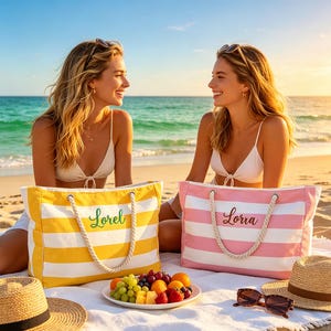 May include: Two personalized beach tote bags, one yellow and white striped with "Lorel" in green script, the other pink and white striped with "Lorra" in brown script. Both have rope handles. A plate of fruit and sunglasses are also visible.