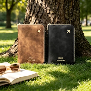 May include: Two rectangular passport holders with gold-tone zippers, one brown and one black. Each features a small gold airplane icon at the top and the text "PASSPORT" with a name, "Axel" or "Hank," printed in gold lettering on the front.