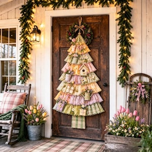 Puede incluir: Un adorno de pared con forma de árbol de Navidad, confeccionado con capas de tela con volantes en tonos pastel de rosa, amarillo y verde. Está decorado con casas para pájaros en miniatura, regaderas y cajas de regalo, rematado con una pequeña corona.