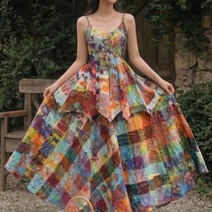 Op de afbeelding: Een kleurrijke tie-dye maxi-jurk met spaghettibandjes en een patchwork rok. De jurk heeft een V-hals en een taille met trekkoord. Een kleine rieten mand met een witte voering staat onderaan de afbeelding. De jurk heeft een mix van kleuren.